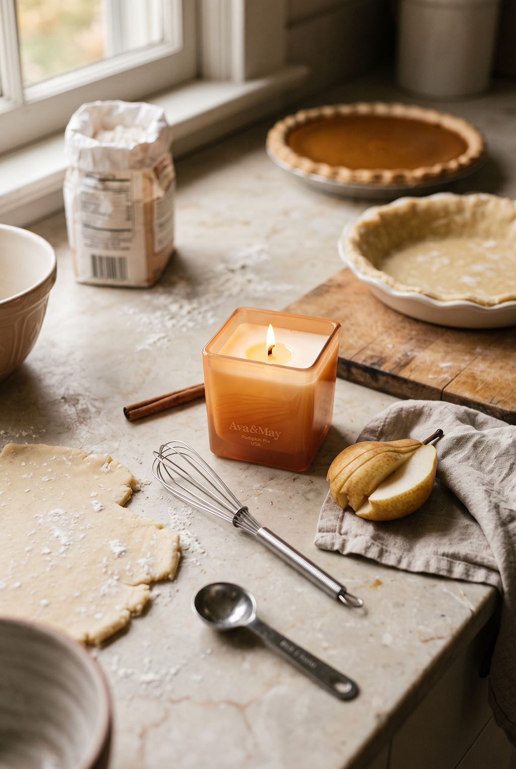 Bougie Ava&May Pumpkin Pie de 220 grammes posée sur le plan de travail de la cuisine, avec de la pâte brisée pour une tarte à la citrouille en cours de préparation, des ustensiles et des poires